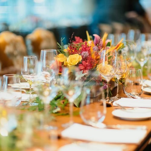 Event image showing a table laid for a dinner with cutlery, napkins, utensils and lovely red and yellow flowers
